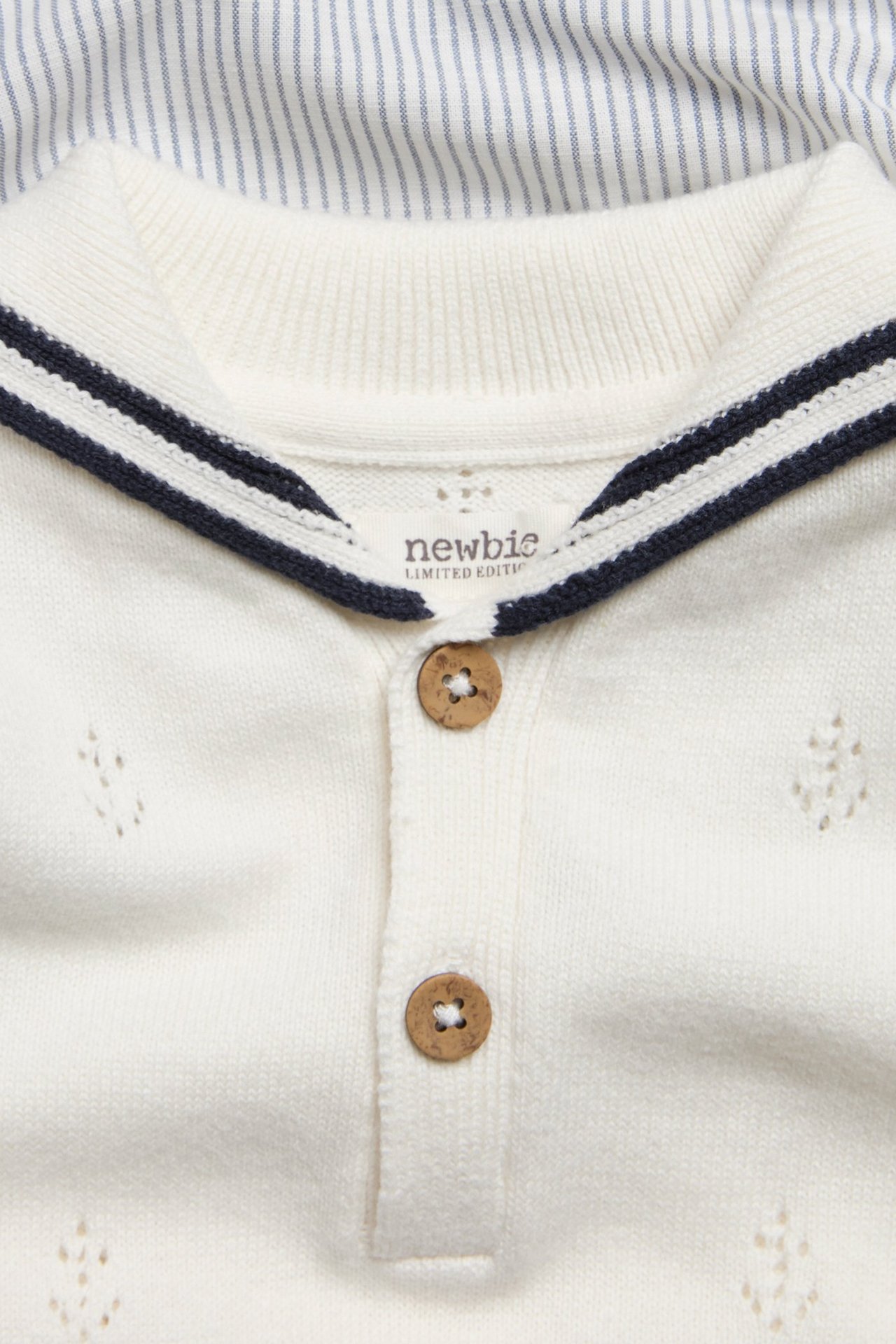 Zbliżenie: kremowy pajacyk niemowlęcy z kotwicami pointelle, pasiastym kołnierzem marynarskim i drewnianymi guzikami.