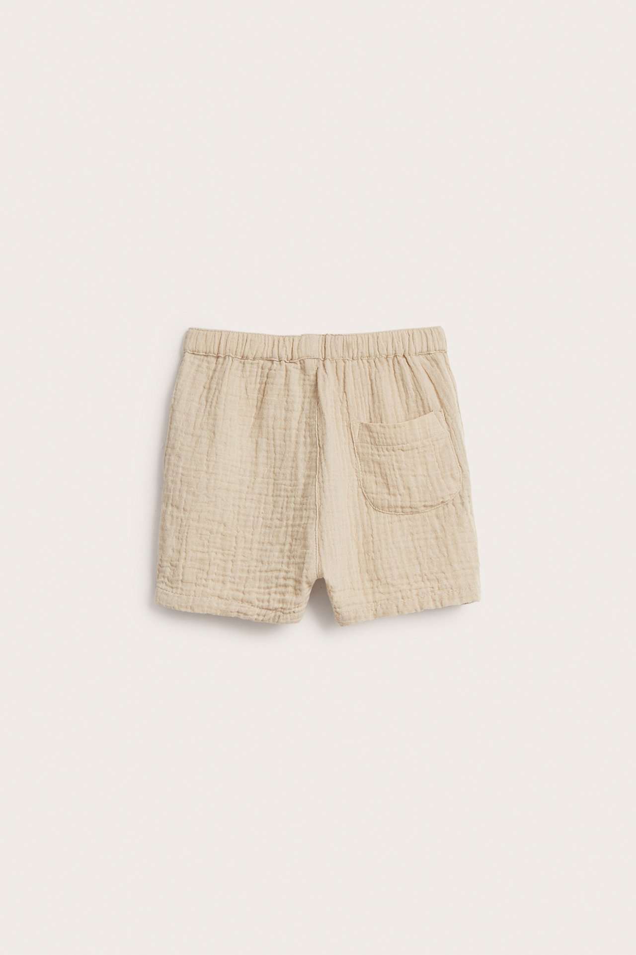 Bakfra: Lysebeige babyshorts i krøllet bomullsmuslin med elastisk midje og baklomme.