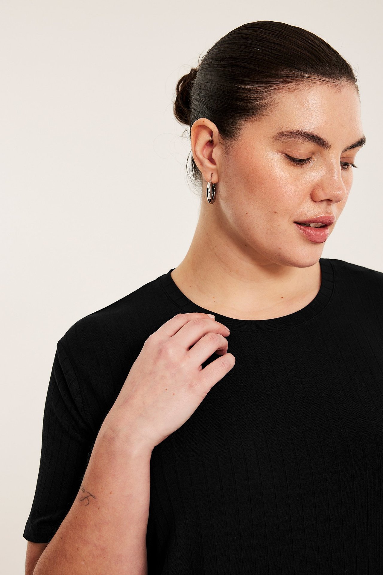 Närbild framifrån av en kvinna i svart ribbad t-shirt och silverfärgade ringörhängen.