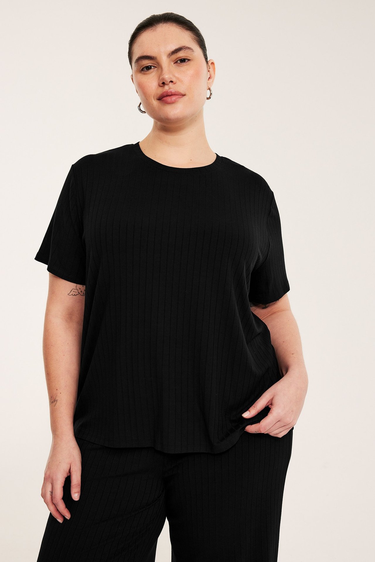 Framifrån: kvinna i svart, boxig, rak ribbad t-shirt och matchande svarta ribbade byxor.