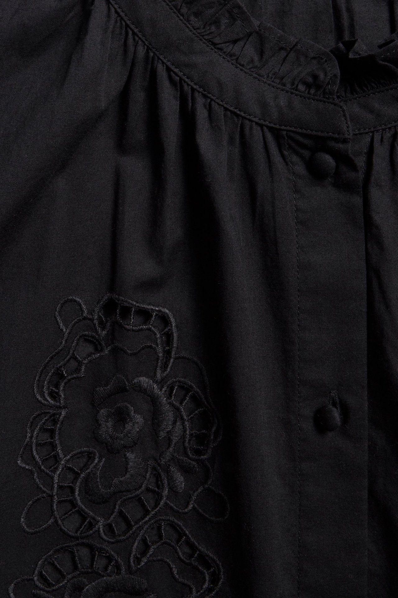 Zbliżenie przodu czarnej bawełnianej bluzki z falbankowym dekoltem, guzikami z przodu i haftem kwiatowym.