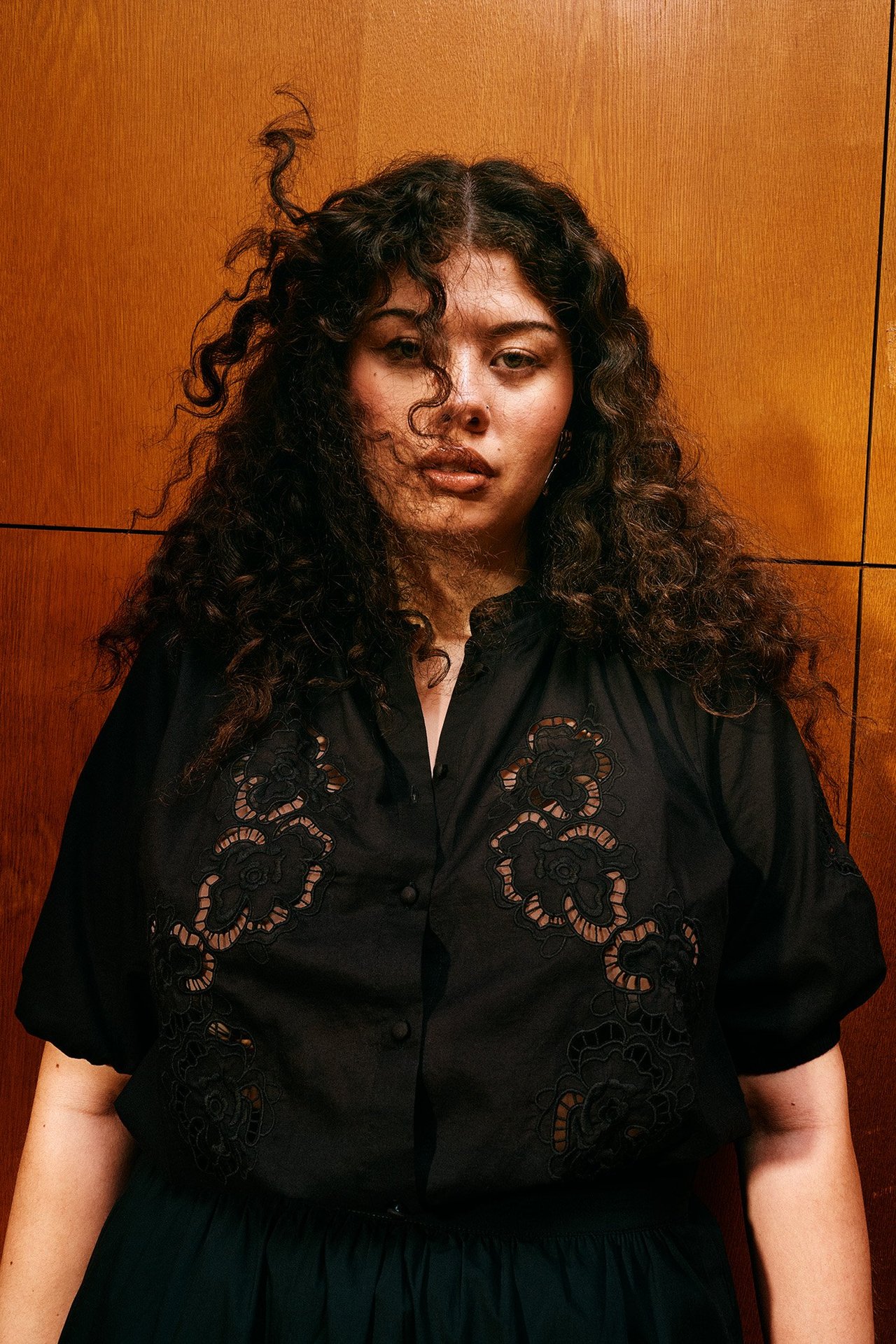 Widok z przodu kobiety w czarnej bawełnianej bluzce z haftem ażurowym i krótkimi rękawami, na ciemnej spódnicy.