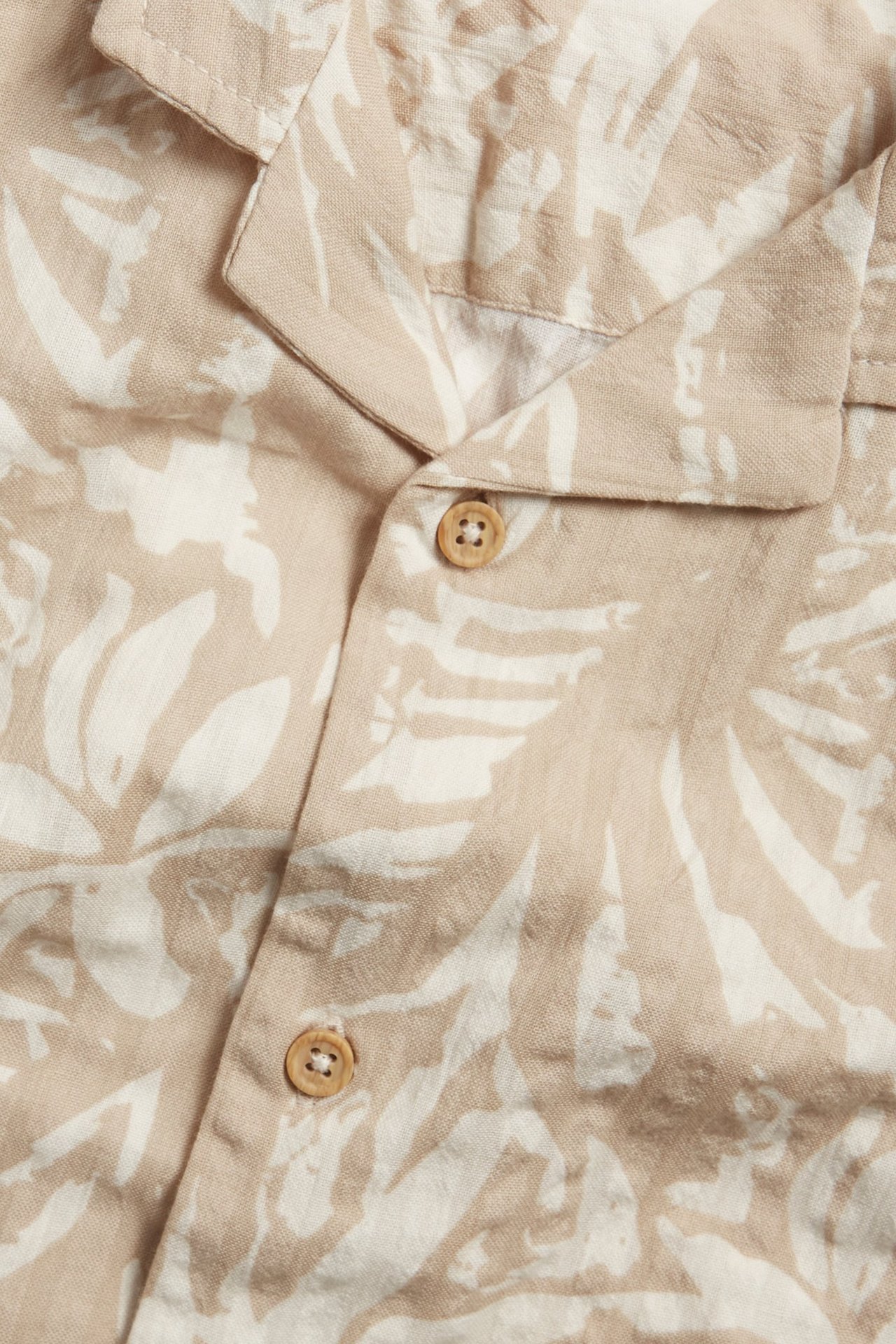 Zbliżenie z przodu: jasnobeżowa koszula z seersuckeru z białym wzorem liści i jasnobrązowymi guzikami.