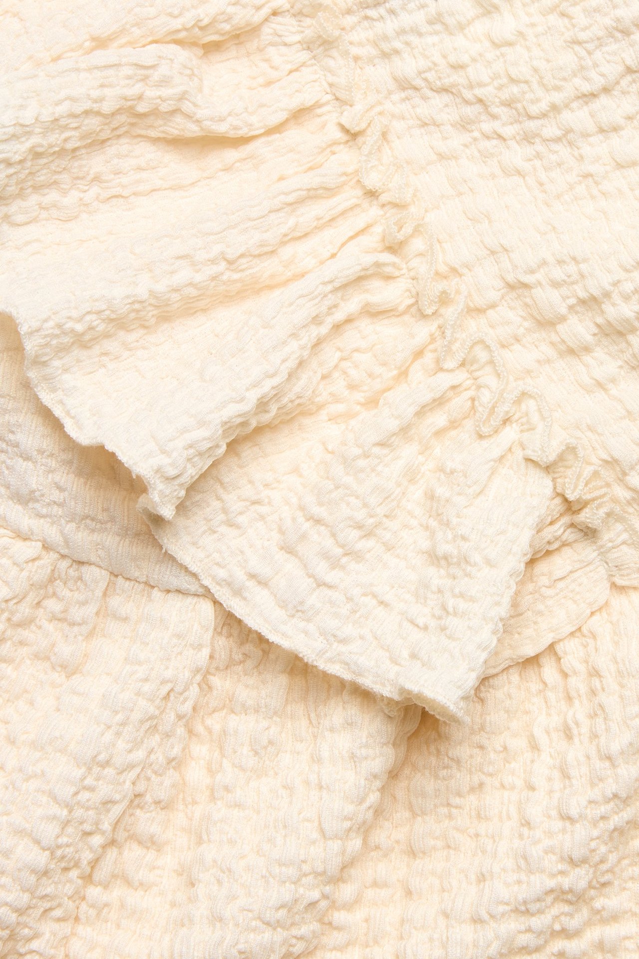 Zbliżenie na kremowy, strukturalny top z dżerseju z dużymi falbanami.