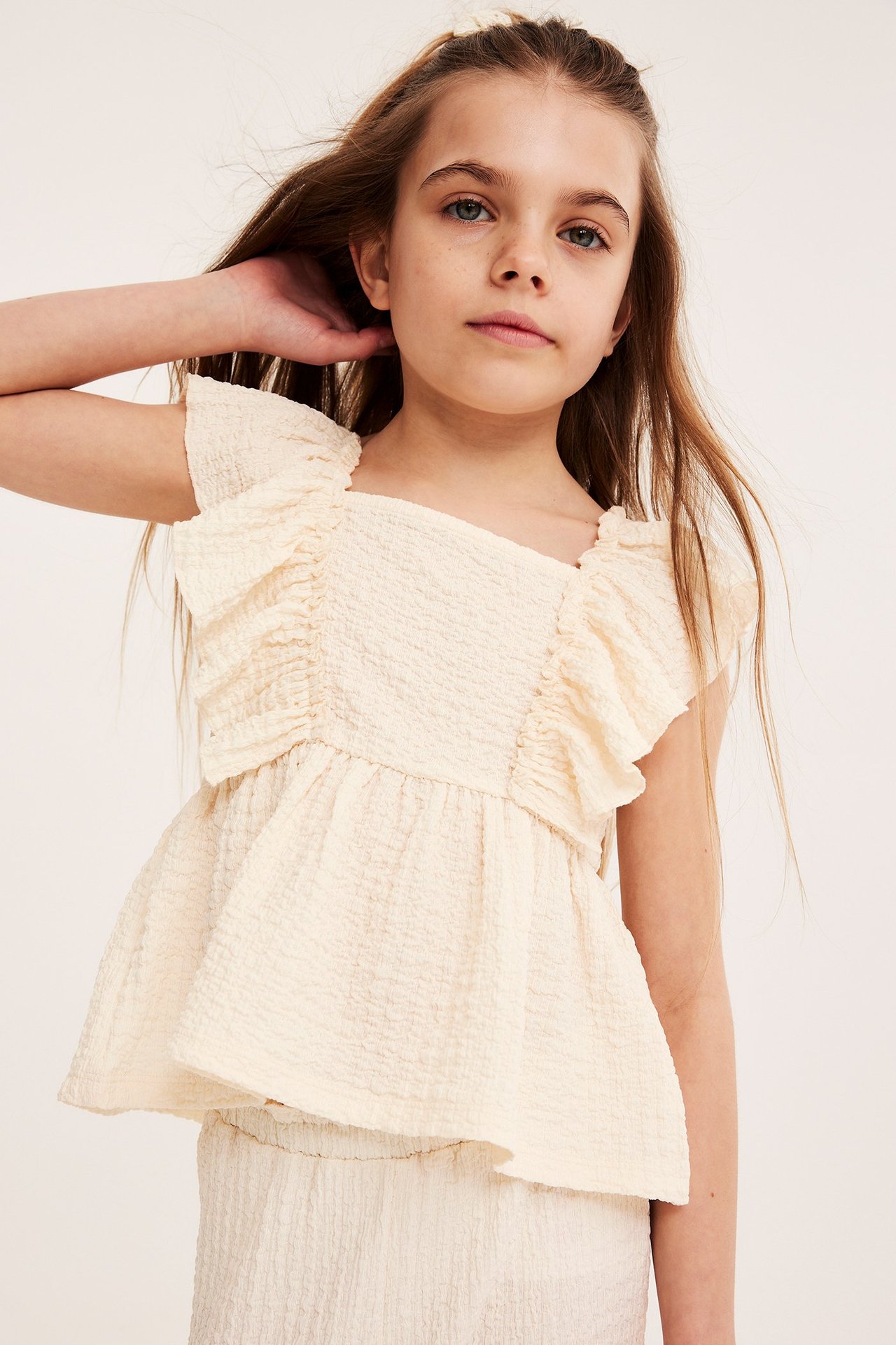Widok z przodu dziecka w kremowym topie z falbanami z teksturowanej dzianiny i pasującym dole.