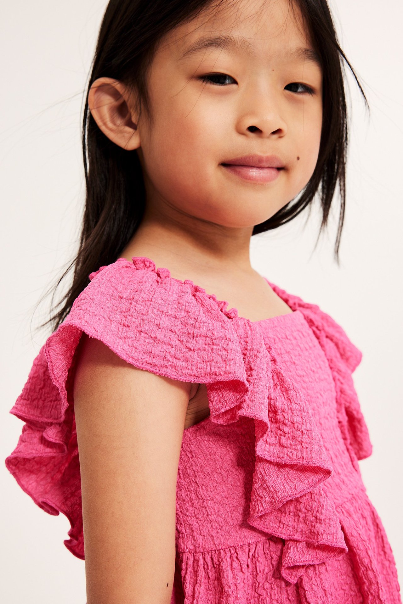 Zbliżenie z przodu na dziecko w różowym topie z teksturowanej dzianiny z dużymi falbanami.