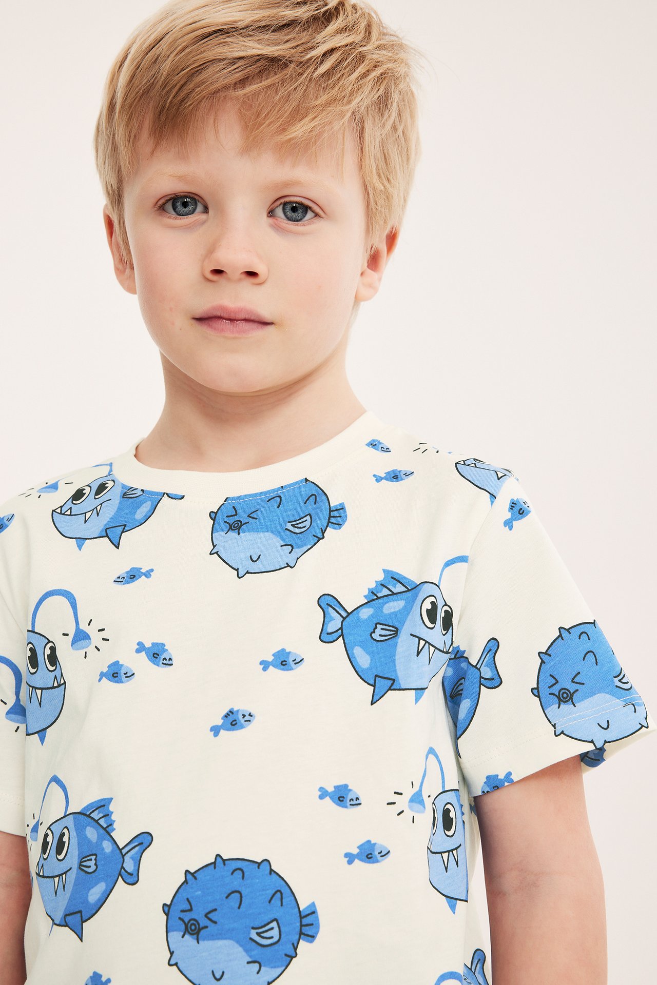 Närbild framifrån på ett barn i en offwhite bomulls-t-shirt med blått fiskmönster.
