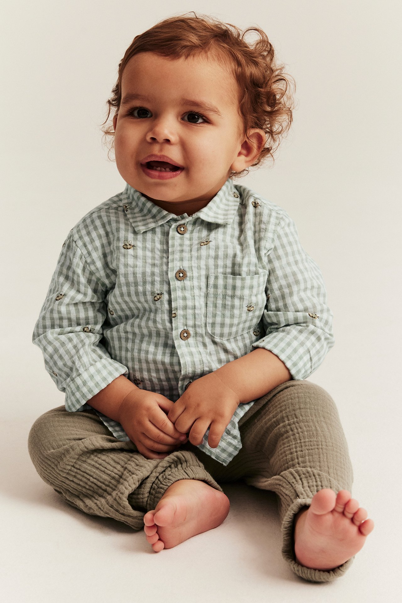 Widok z przodu: dziecko w jasnozielonej koszuli w kratkę z pszczółkami z seersuckeru i oliwkowych marszczonych spodniach.