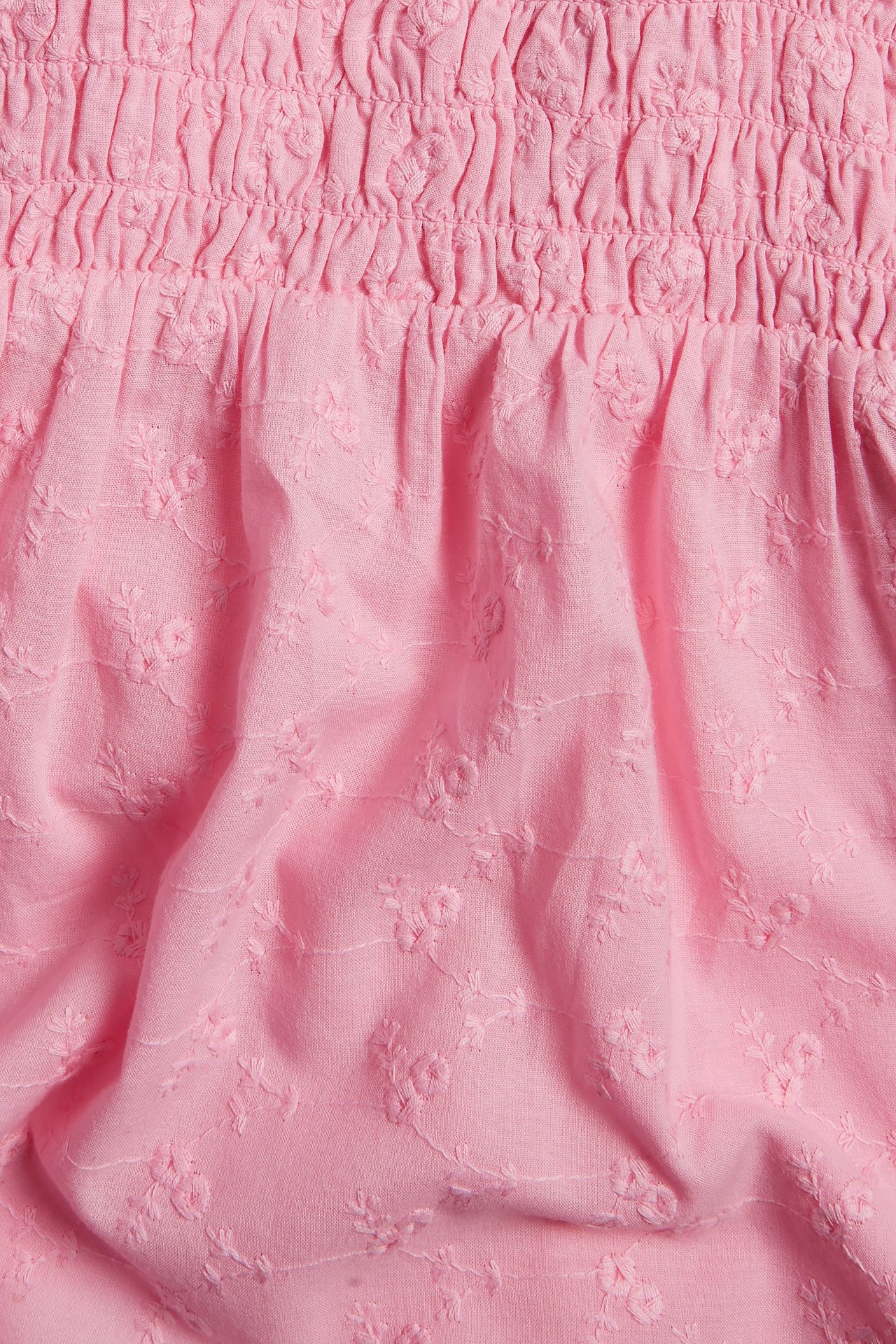 Zbliżenie różowego topu z tkanej bawełny ze smockiem i kwiatowym haftem.