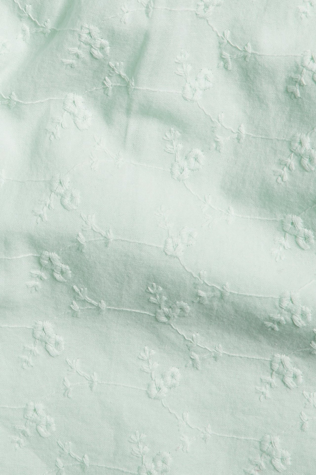 Zbliżenie na jasnozielony bawełniany materiał szortów z białym haftem kwiatowym.