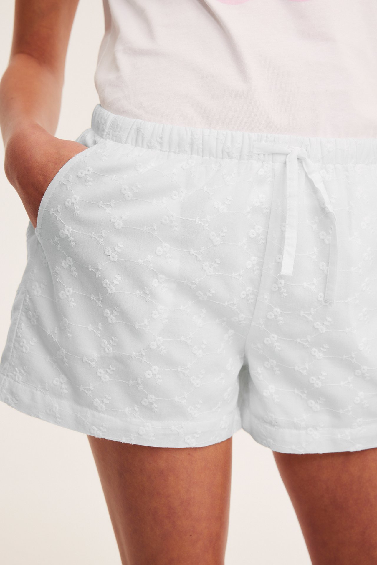 Närbild framifrån på barn i vita broderade bomullsshorts med dragsko i midjan och en vit t-shirt.