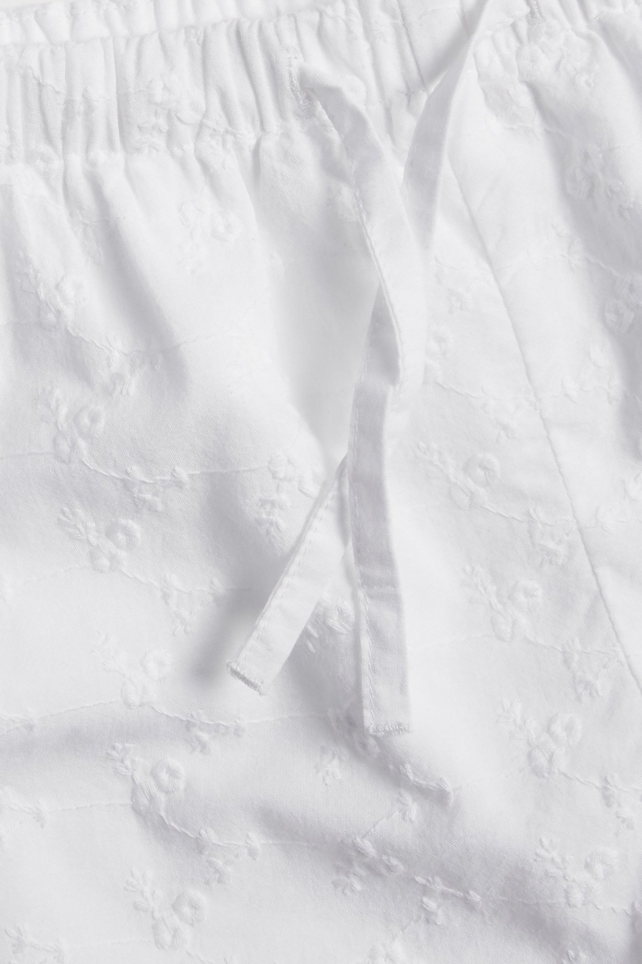 Zbliżenie na białe, haftowane bawełniane szorty z elastycznym pasem ze sznurkiem.