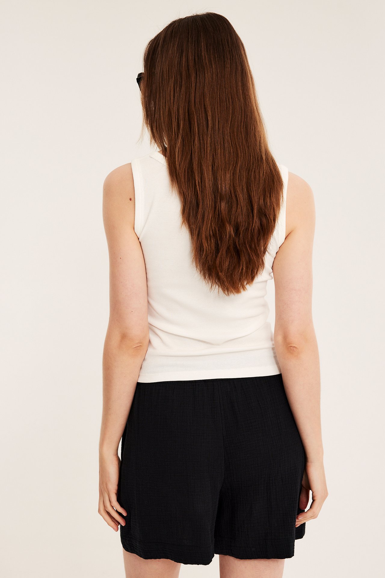 Nainen takaapäin, yllään mustat strukturoidut puuvillashortsit ja kermanvärinen hihaton toppi.