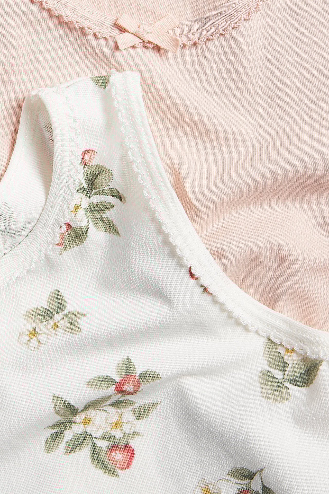 Närbild av ett offwhite blommigt baby-linne med uddkanter, och ett rosa linne med rosett.