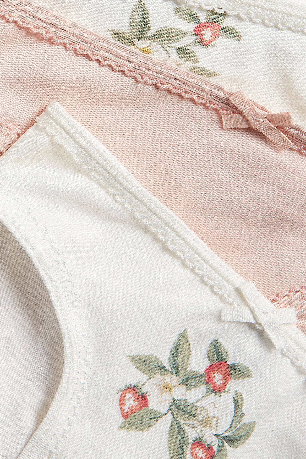 Närbild på tre trikåtrosor: två offwhite med jordgubbsmönster, en ljusrosa, med rosetter och uddkanter.