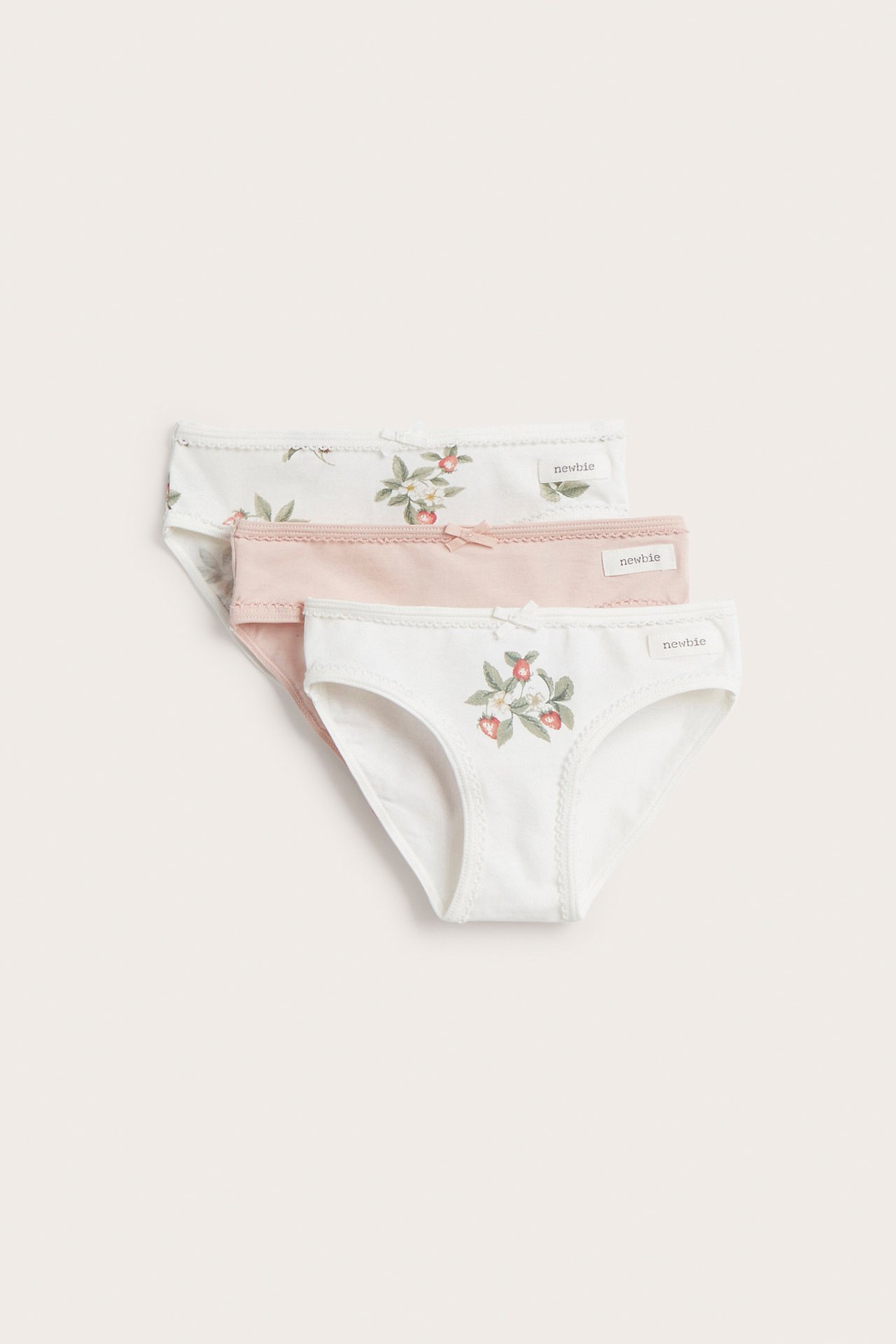 Frontvy av tre barntrosor i bomull: offwhite med jordgubbsmönster, ljusrosa och offwhite med blommor.