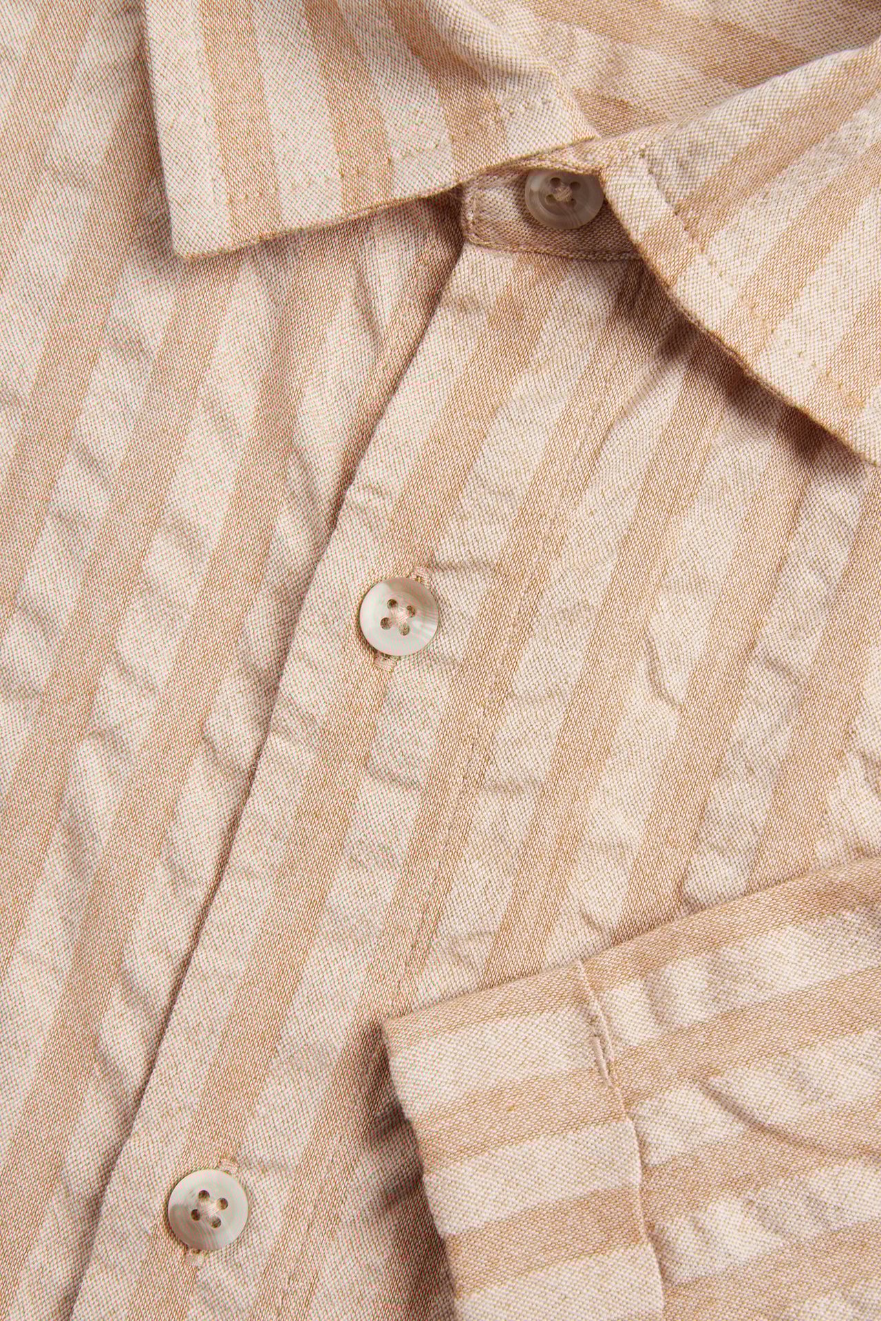 Zbliżenie beżowo-jasnobrązowej, pasiastiej koszuli z krótkim rękawem z seersuckeru, z kołnierzykiem i guzikami.