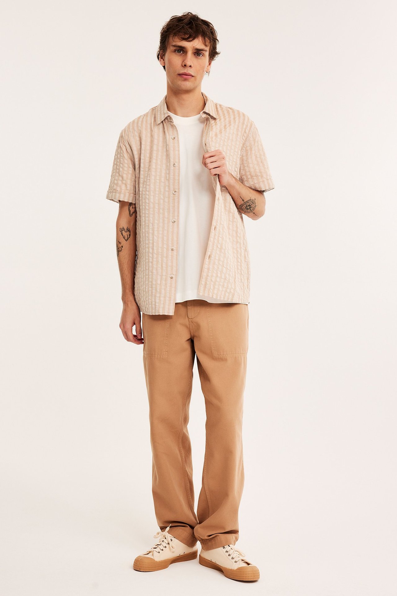 Mies edestä: vaaleanruskea raidallinen seersucker-paita, valkoinen t-paita, ruskeat housut, beiget kengät.