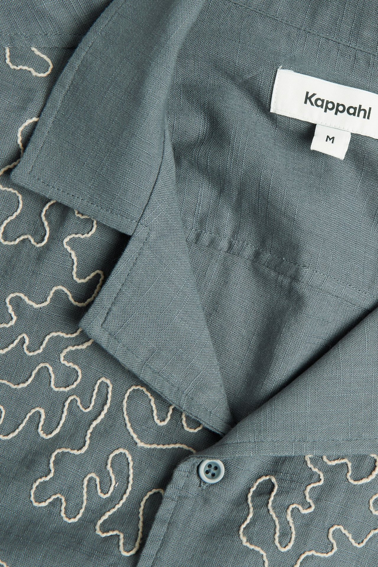 Zbliżenie na ciemnoszarą bawełnianą koszulę resortową z białym haftem i guzikiem.