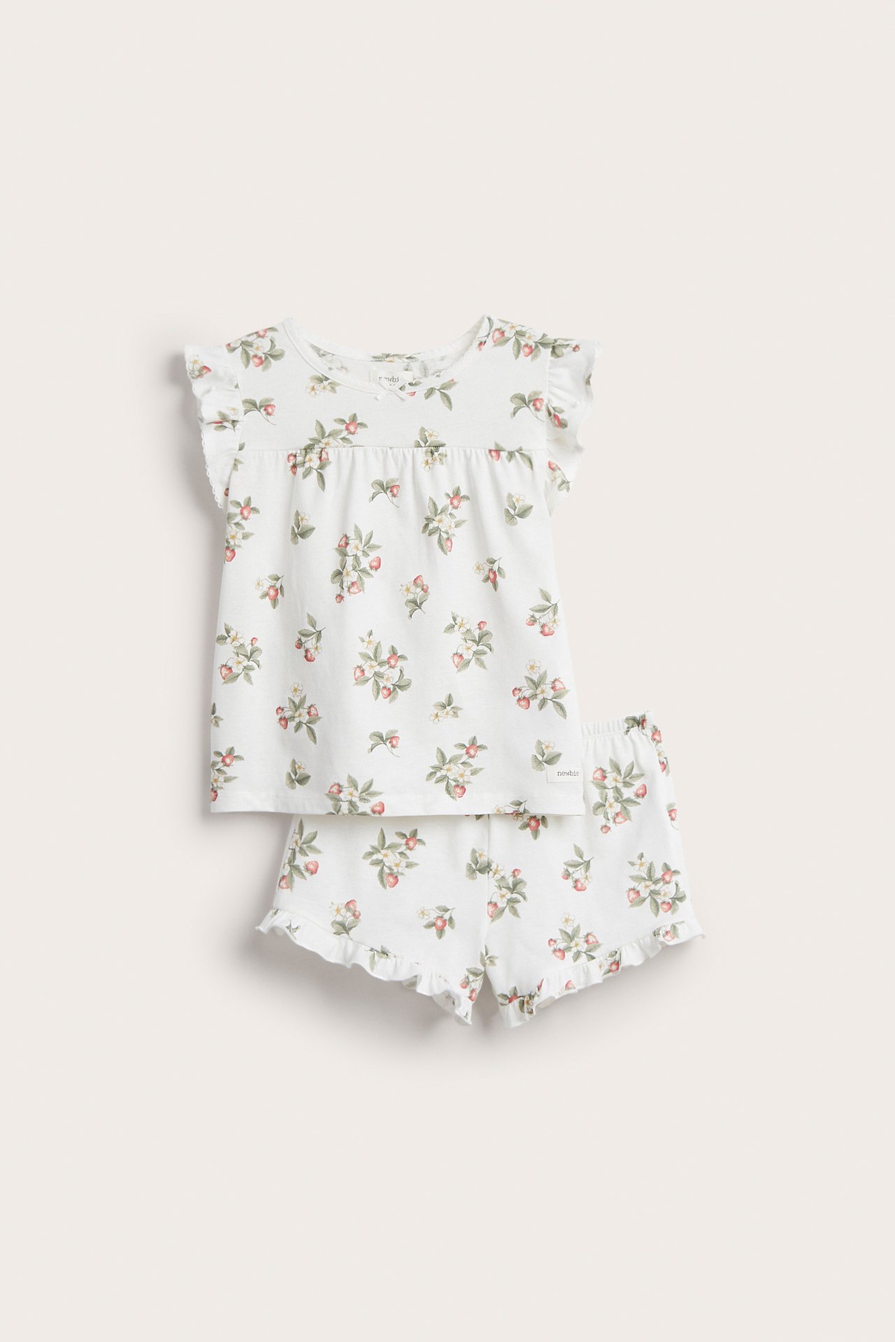 Edestä näkymä luonnonvalkoisesta lasten puuvillapyjamasetistä, jossa mansikkakuvio, röyhelöhihat ja yhteensopivat shortsit.