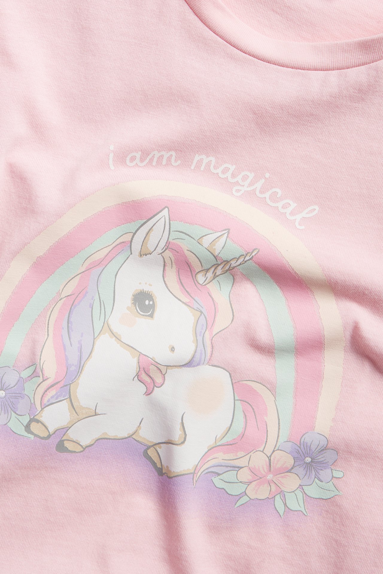Lähikuva edestä: vaaleanpunainen t-paita, jossa värikäs yksisarvinen, sateenkaari ja "i am magical" -teksti.