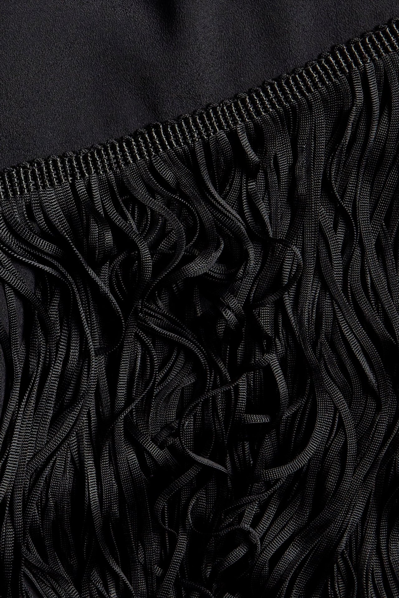 Zbliżenie czarnej poliestrowej sukienki ze szczegółowym frędzlowym obszyciem.
