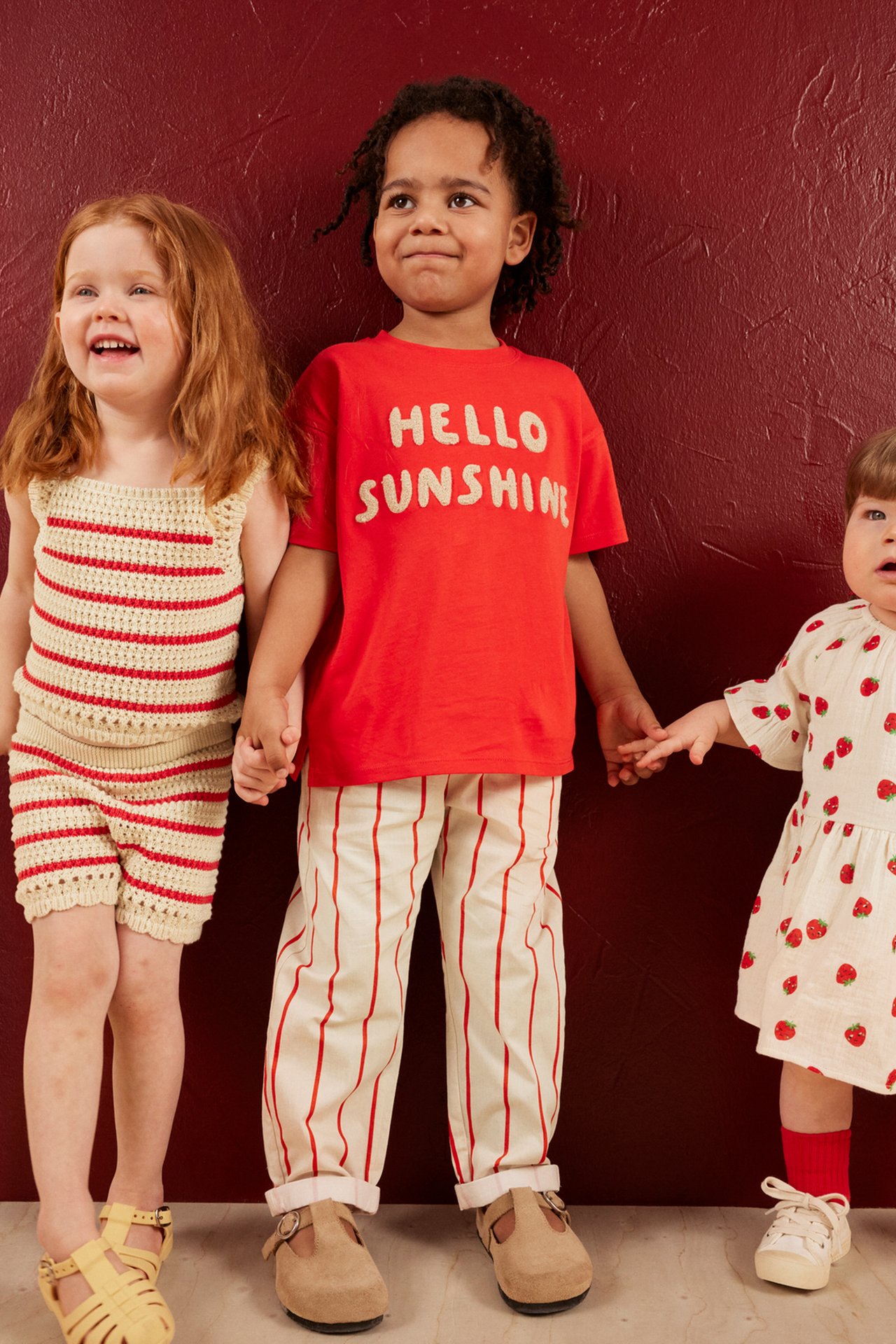 Framifrån: Barn i röd bomulls-t-shirt med 'HELLO SUNSHINE' applikation, randiga byxor. Två barn.