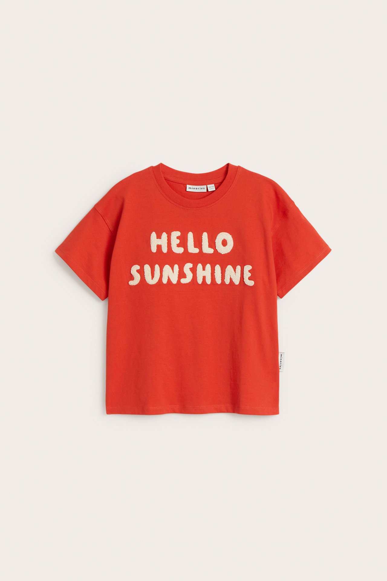 Frontvy av en röd bomulls-t-shirt för barn med gräddvit frottéapplikation 'HELLO SUNSHINE'.