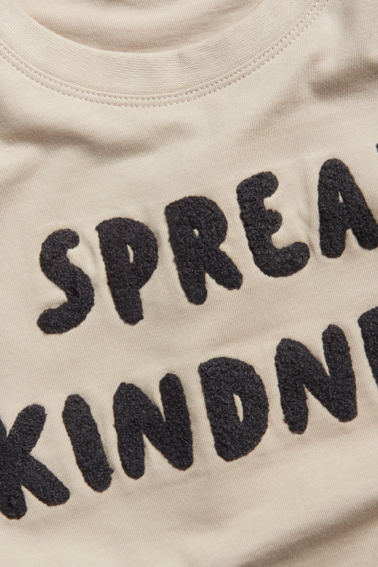 Närbild av en ljusbeige bomulls-t-shirt med svart frottéapplikationstext på framsidan.