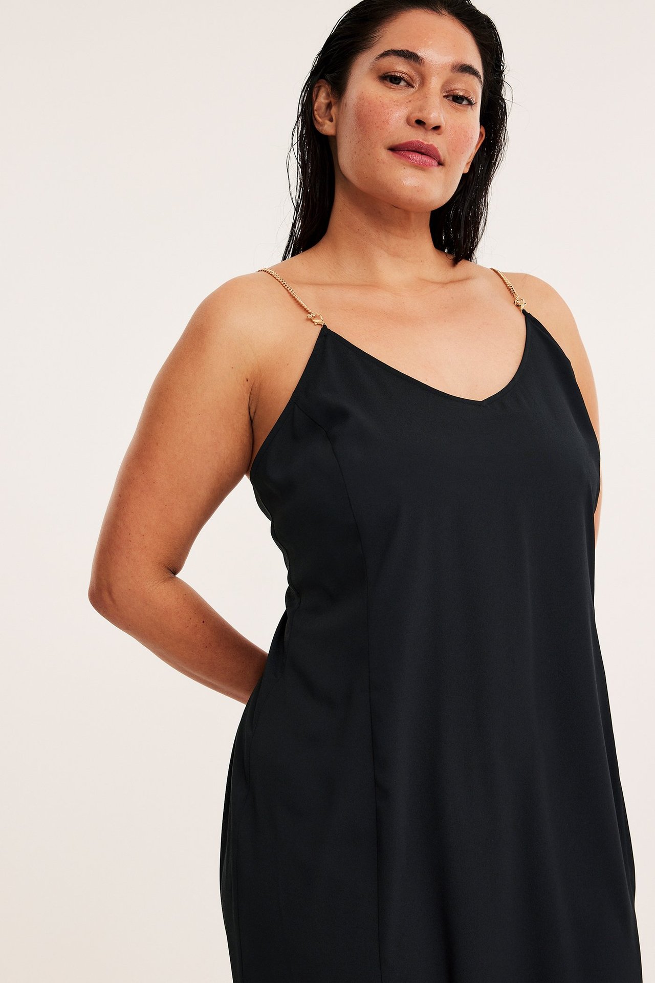 Edestä kuvattu nainen yllään musta polyesterimekko kultaisilla ketjuolkaimilla.