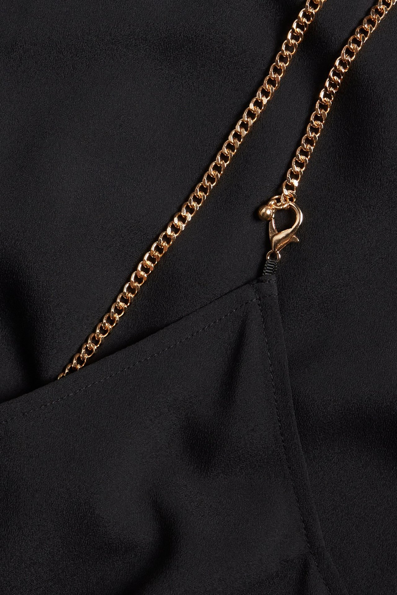 Zbliżenie czarnej sukienki poliestrowej ze złotym łańcuszkiem i zapięciem.