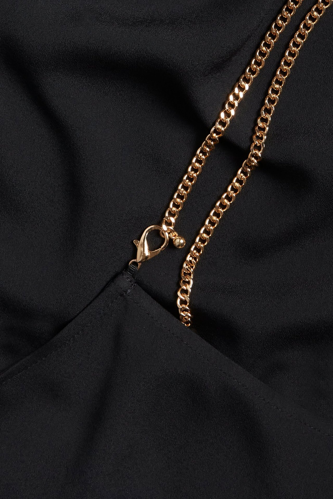 Zbliżenie czarnego topu z poliestru ze złotym łańcuszkiem i zapięciem karabińczykowym.