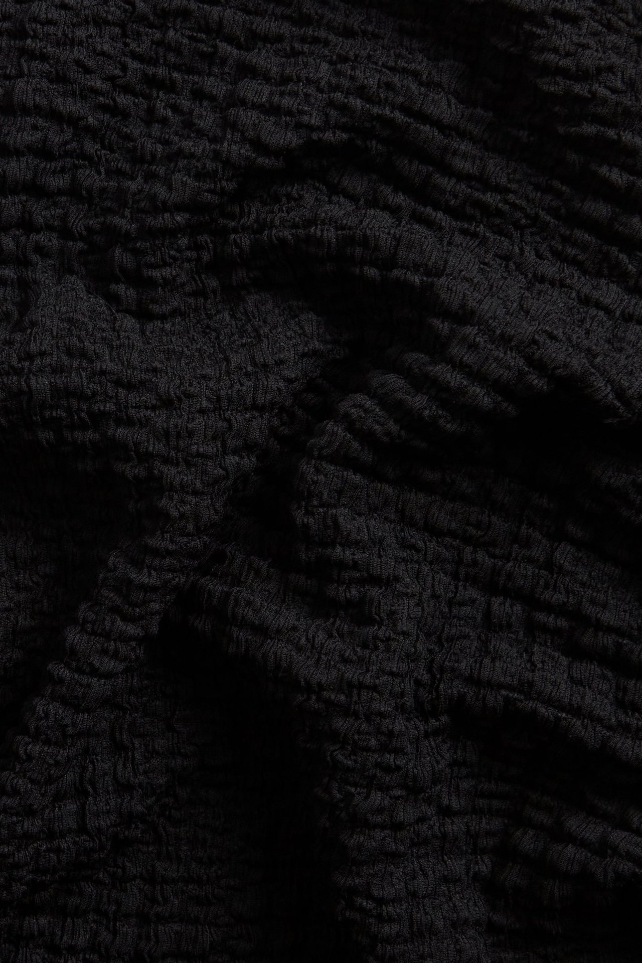 Zbliżenie czarnego, strukturalnego materiału bluzki z długim rękawem.