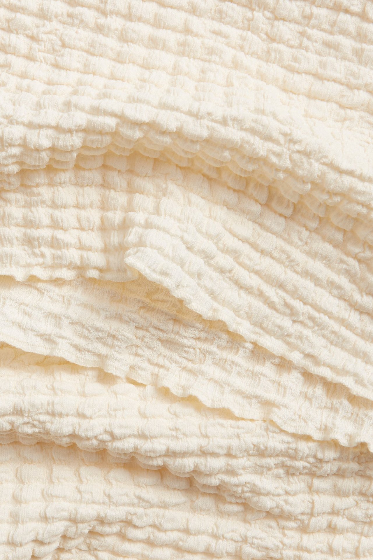 Zbliżenie na biały top z długim rękawem, ukazujące jego teksturowany, pognieciony materiał.