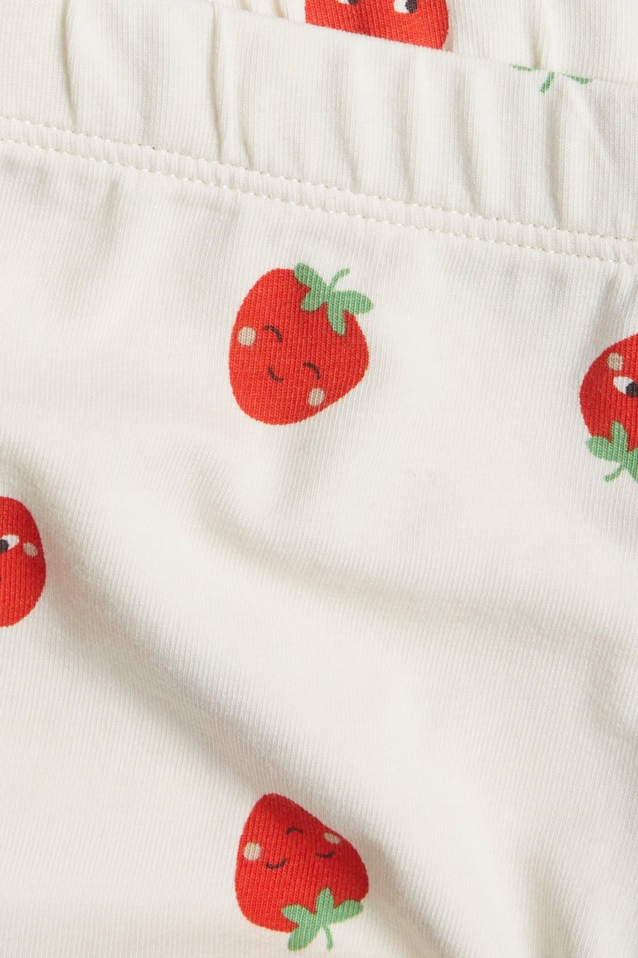 Lähikuva kermanvärisistä vauvan shortseista, joissa on punainen hymyilevä mansikkakuvio ja joustava vyötärö.