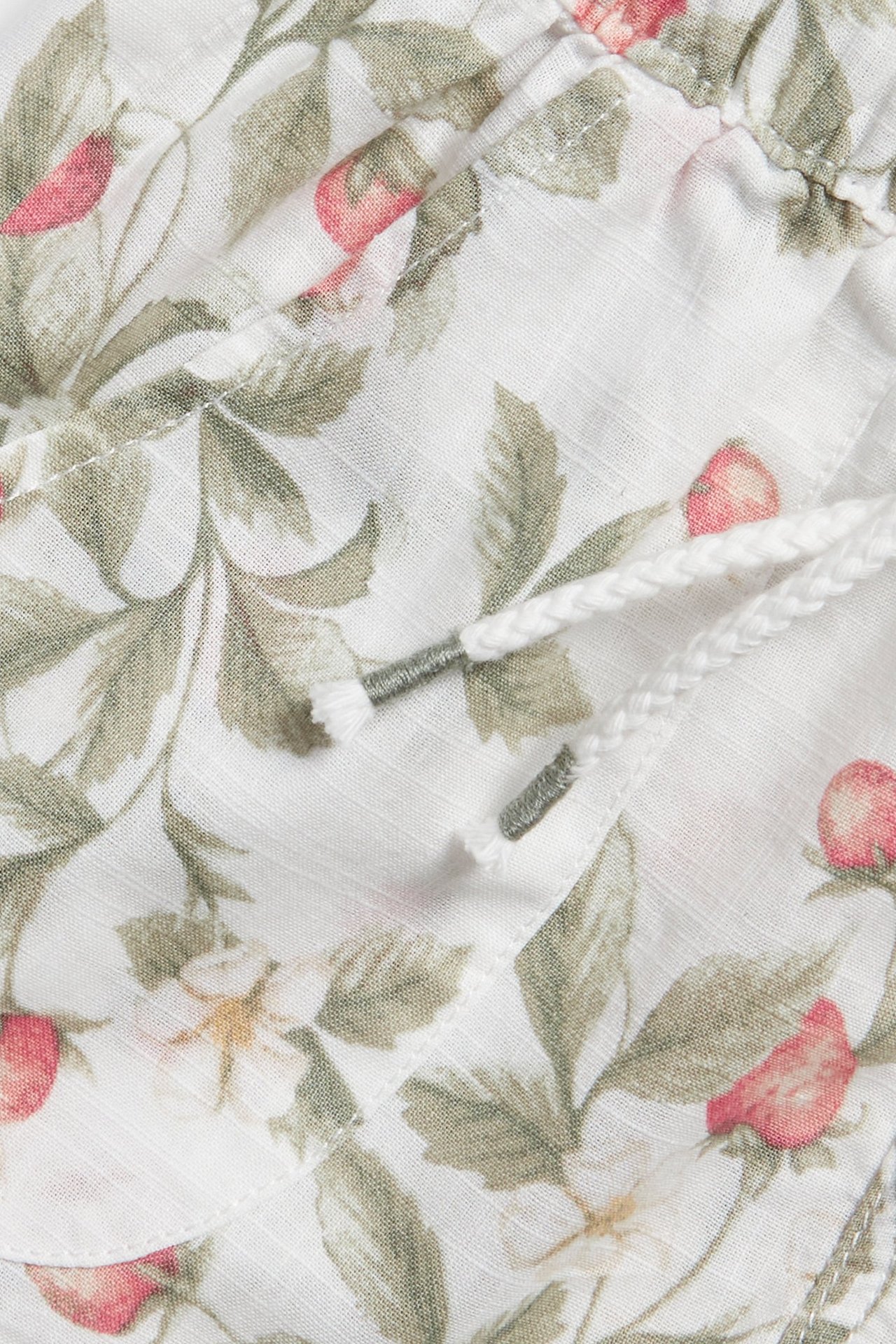 Lähikuva luonnonvalkoisista puuvillashortseista, mansikkakuvio, joustava vyötärö, valkoinen kiristysnyöri.