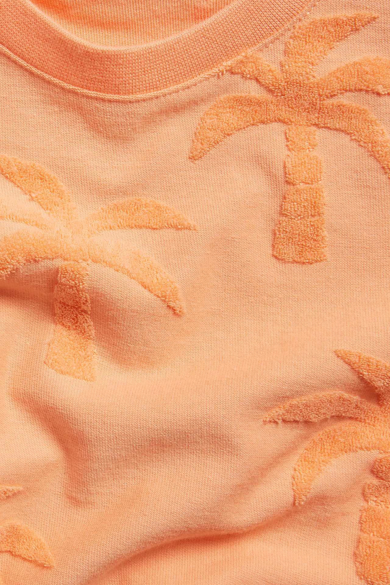 Närbild av en orange t-shirt med texturerade frottépalmmönster och ribbad halsringning.