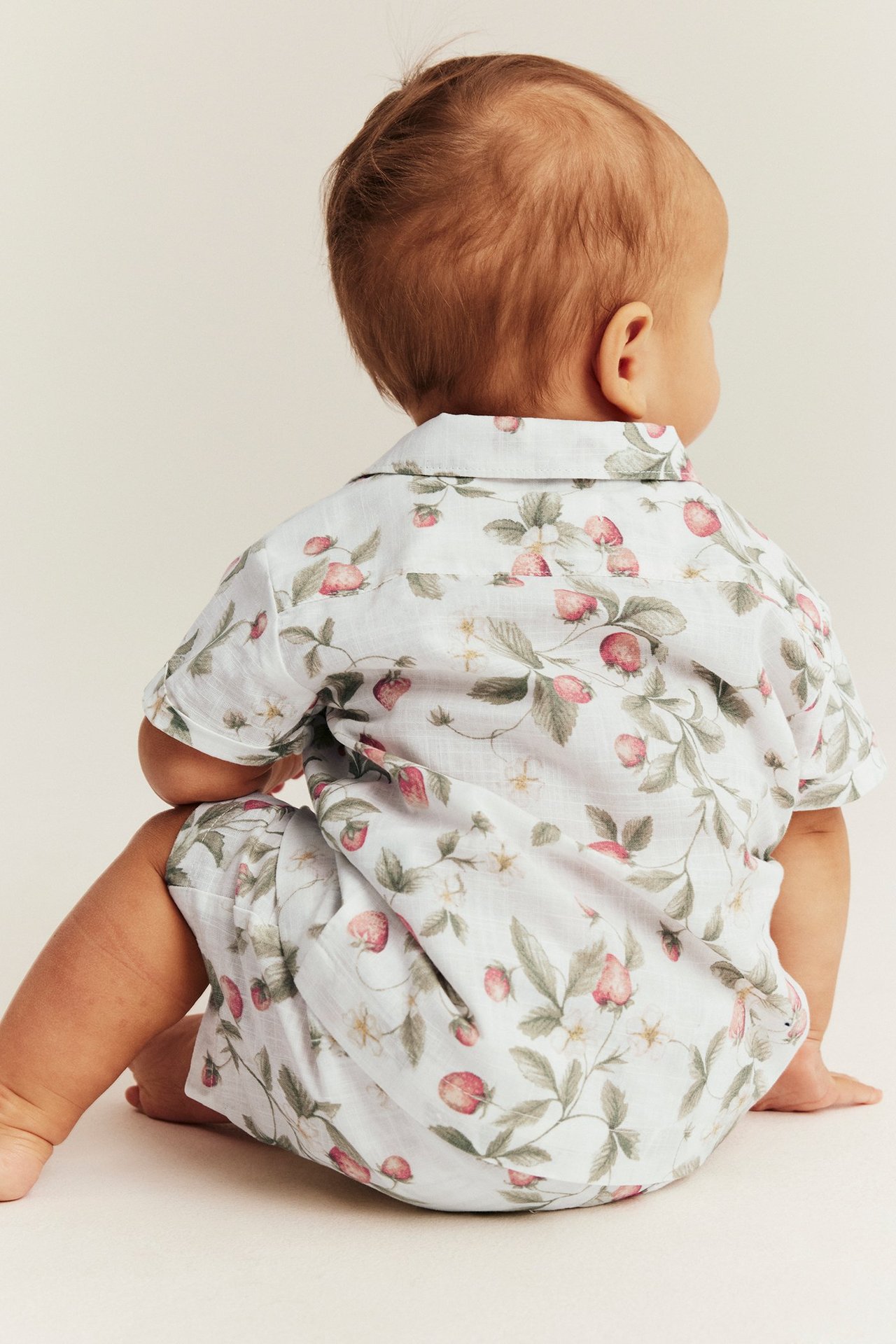 Widok z tyłu dziecka w kremowej bawełnianej koszuli z krótkim rękawem i pasujących szortach w truskawki.