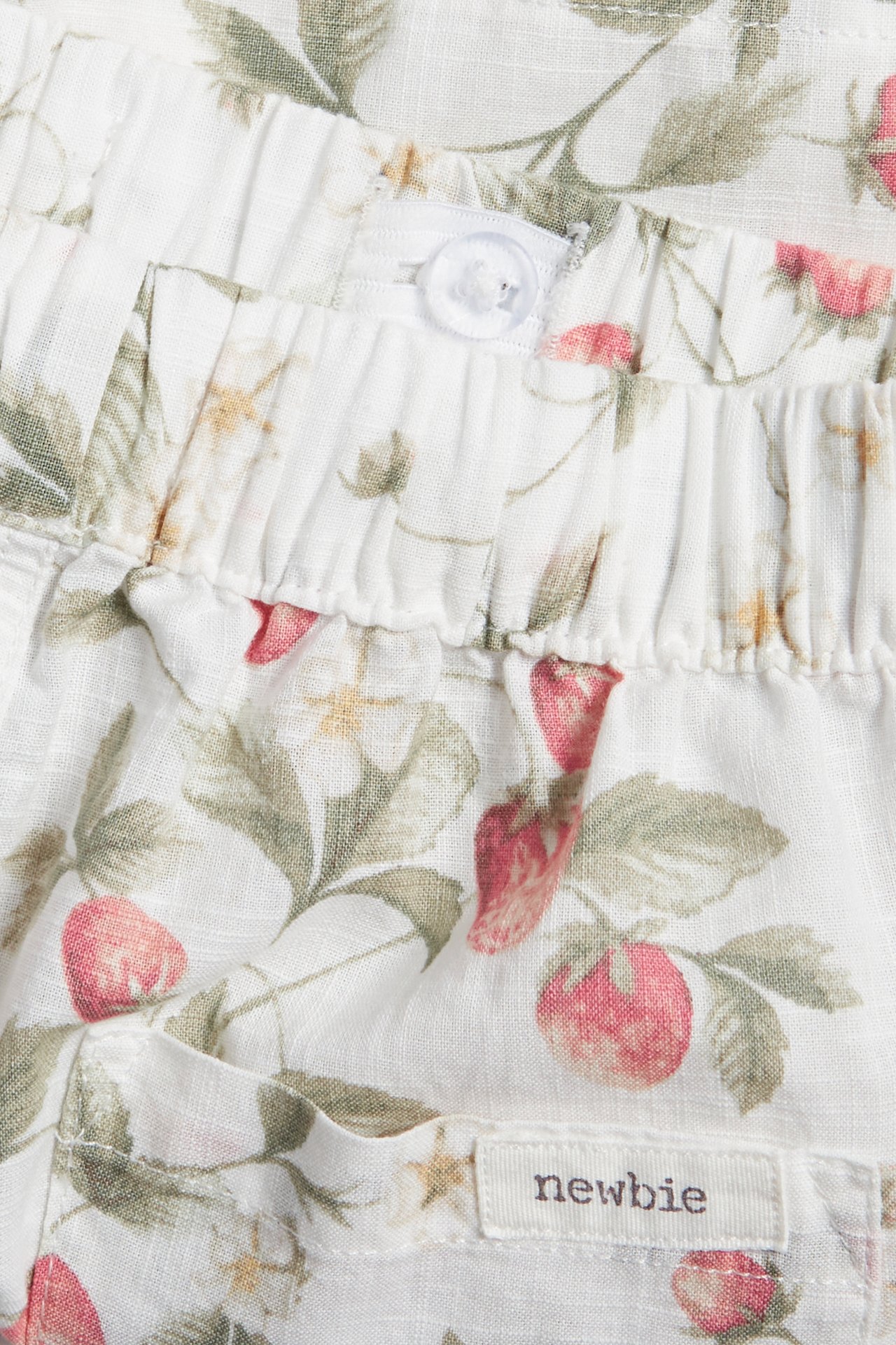 Närbild av offwhite bomullsshorts med rött jordgubbsmönster, resår i midjan och en genomskinlig knapp.