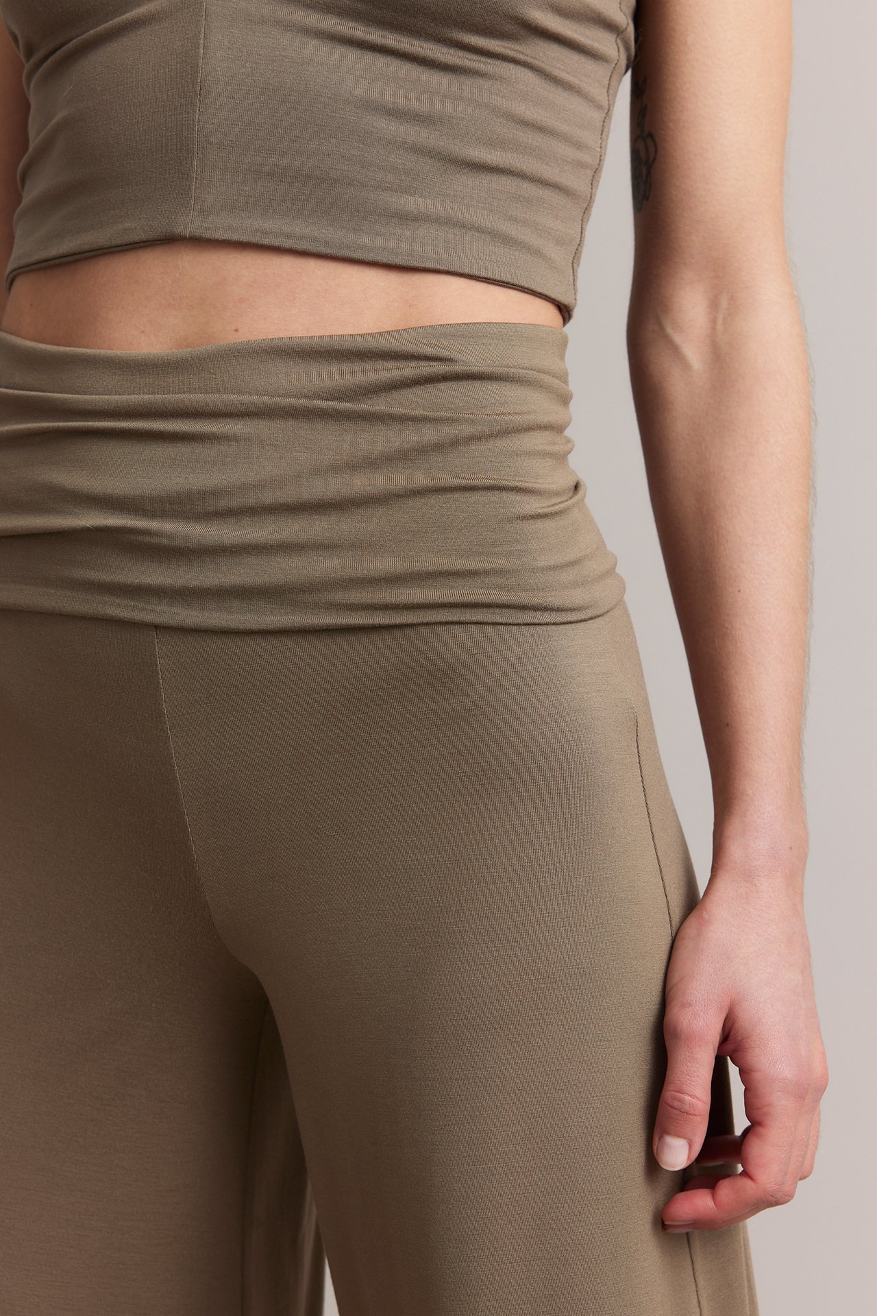 Zbliżenie kobiety w brązowych szerokich spodniach loungewear z wywijanym pasem i pasującym topem crop.