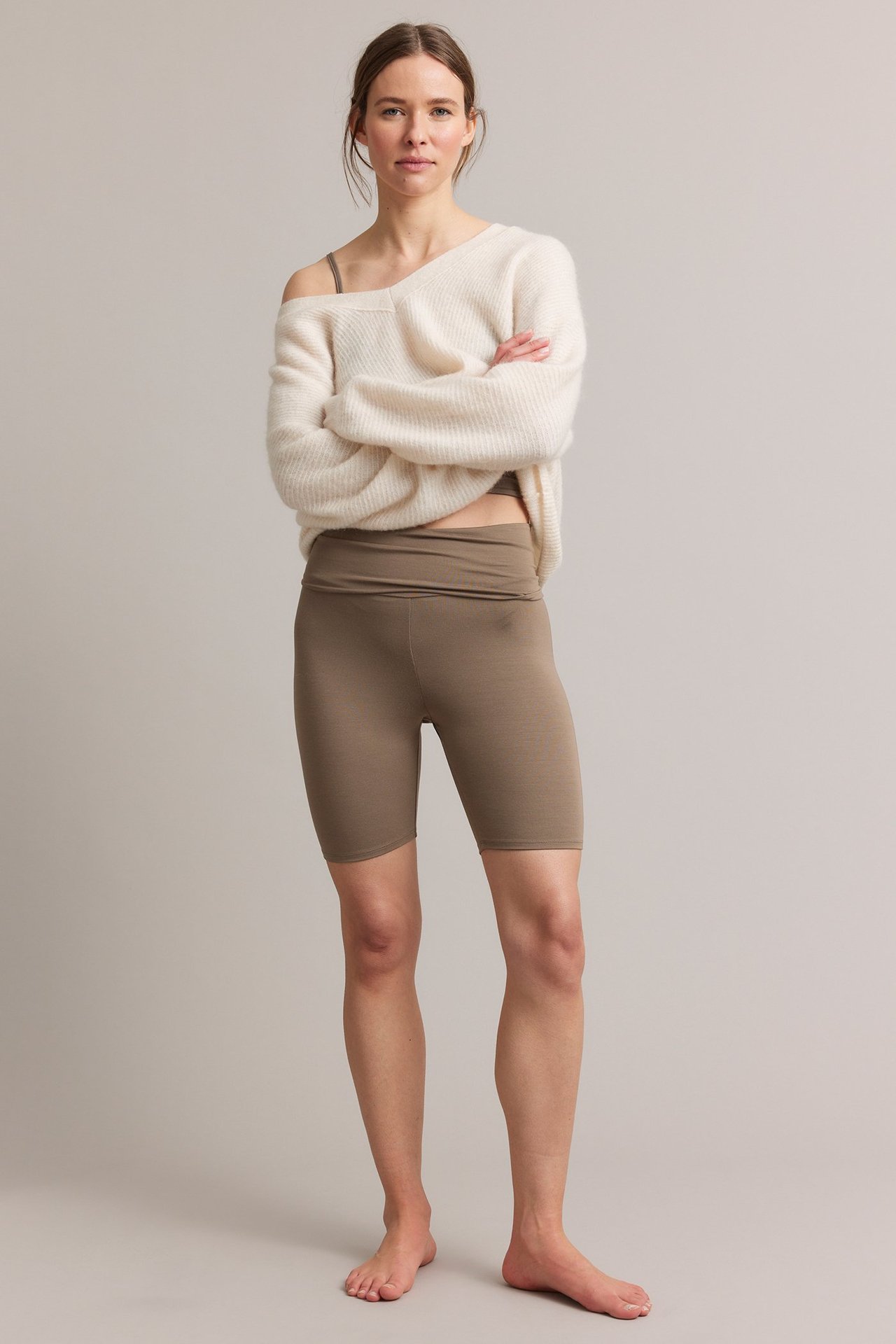 Framifrån: Kvinna i bruna cykelbyxor med nervikbar midja, brun BH och en benvit tröja.