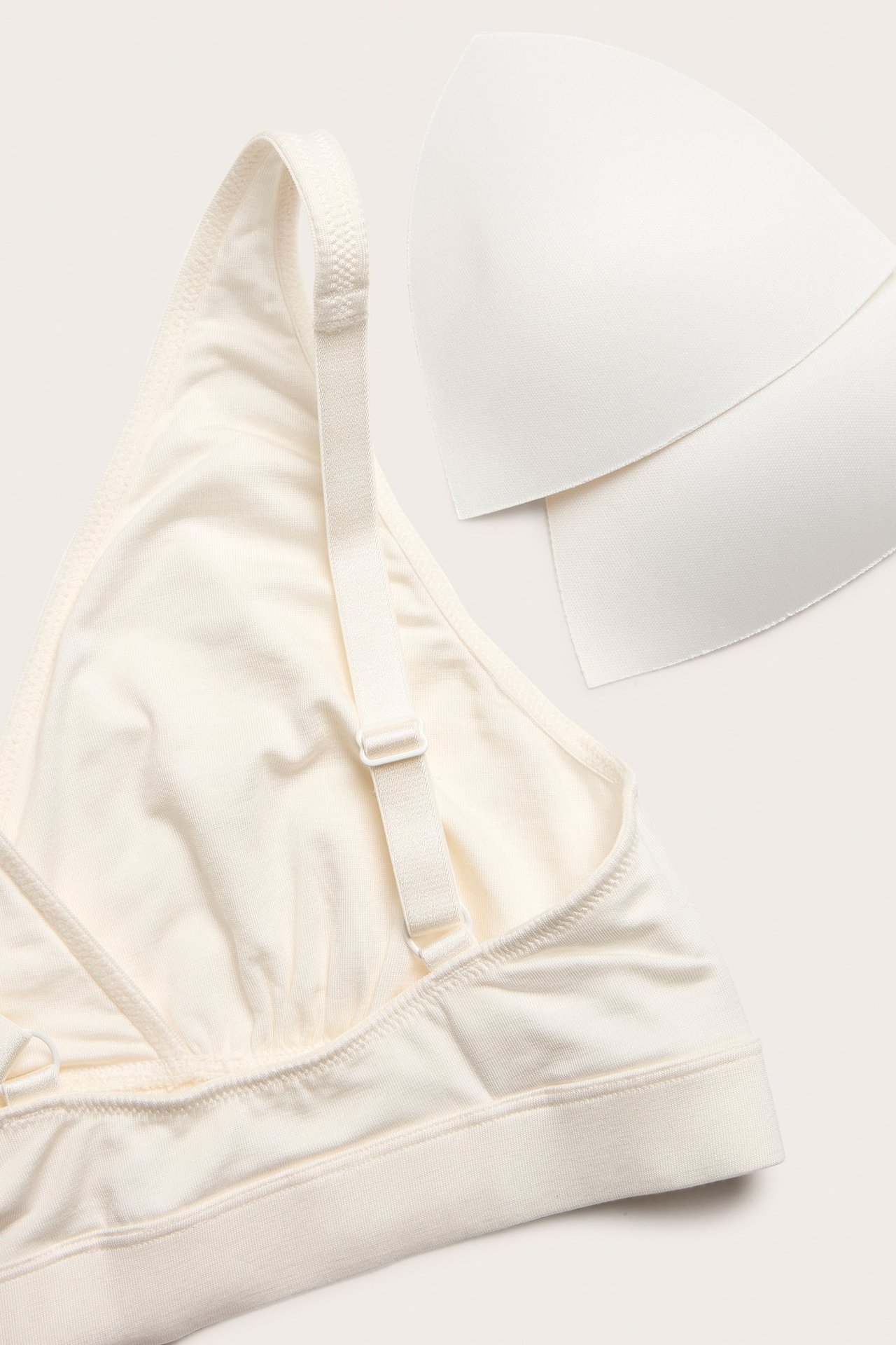 Zbliżenie białego, miękkiego topu biustonosza z regulowanymi ramiączkami i dwoma białymi wkładkami.