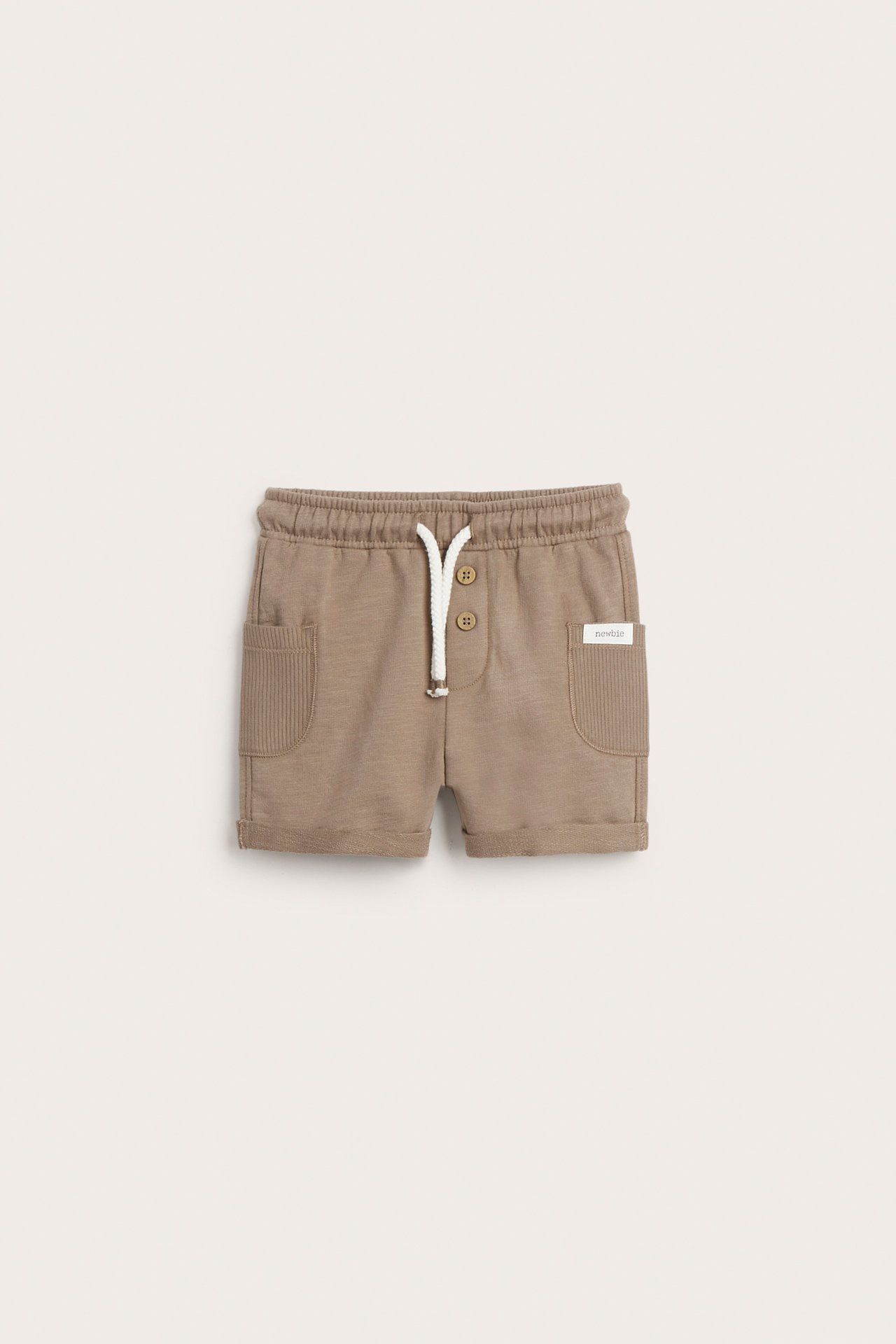 Frontvisning av brune baby-shorts i slub-jersey med elastisk midje, hvit snøring, knapper og ribbestrikkede lommer.