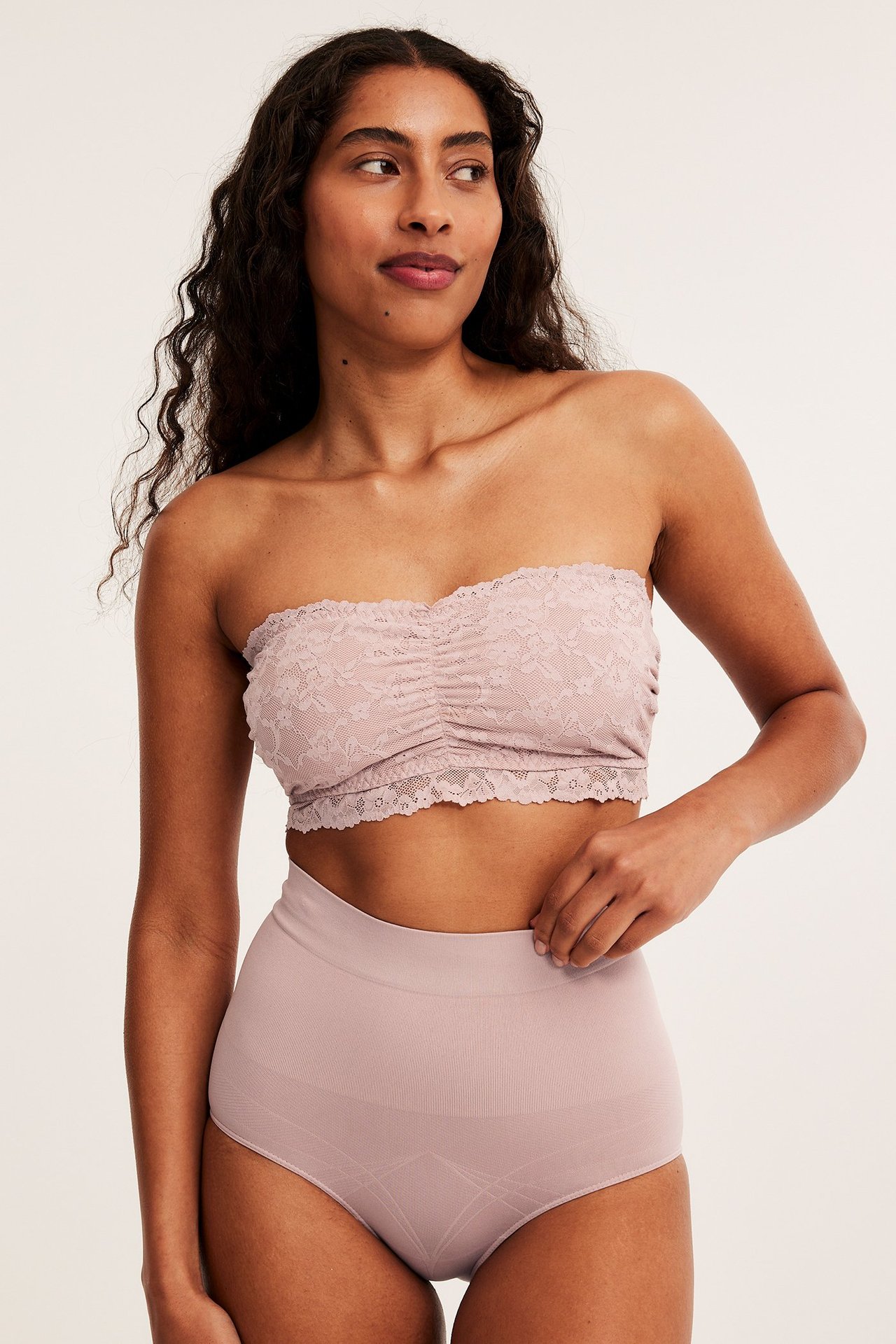 Forfra, kvinne i lys rosa høytlivs shapingtruse og matchende blonde bandeau-bh.
