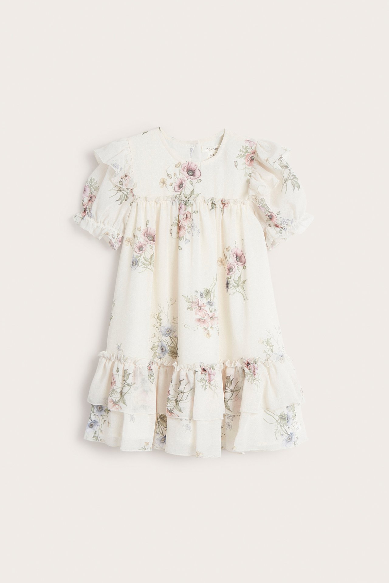 Frontvisning av en offwhite blomstret chiffonkjole for barn med puffermer, volanger og etasjeskjørt.