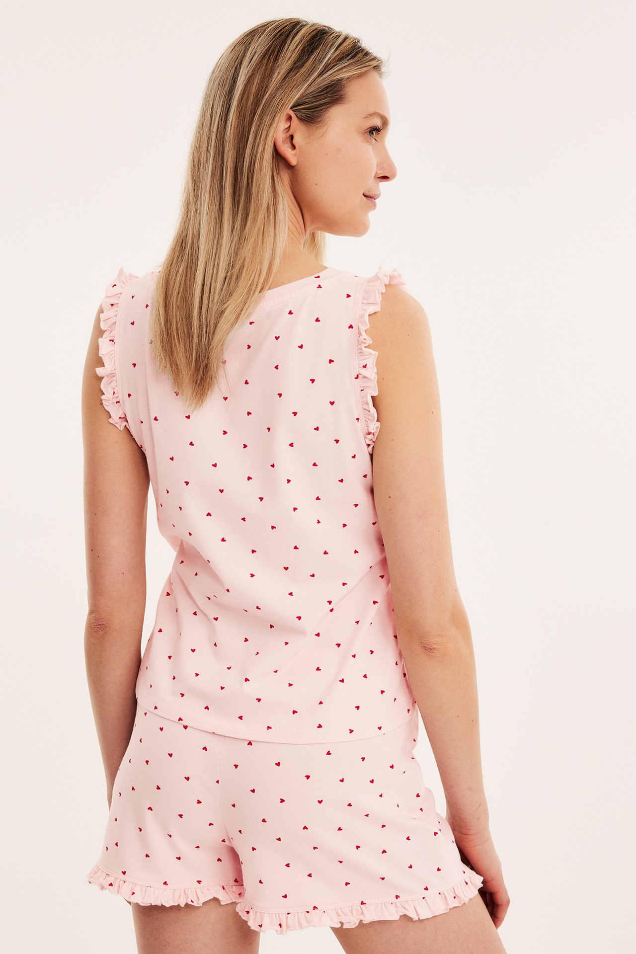 Bakifrån: kvinna i rosa pyjamasset med röda hjärtan och volangkanter.