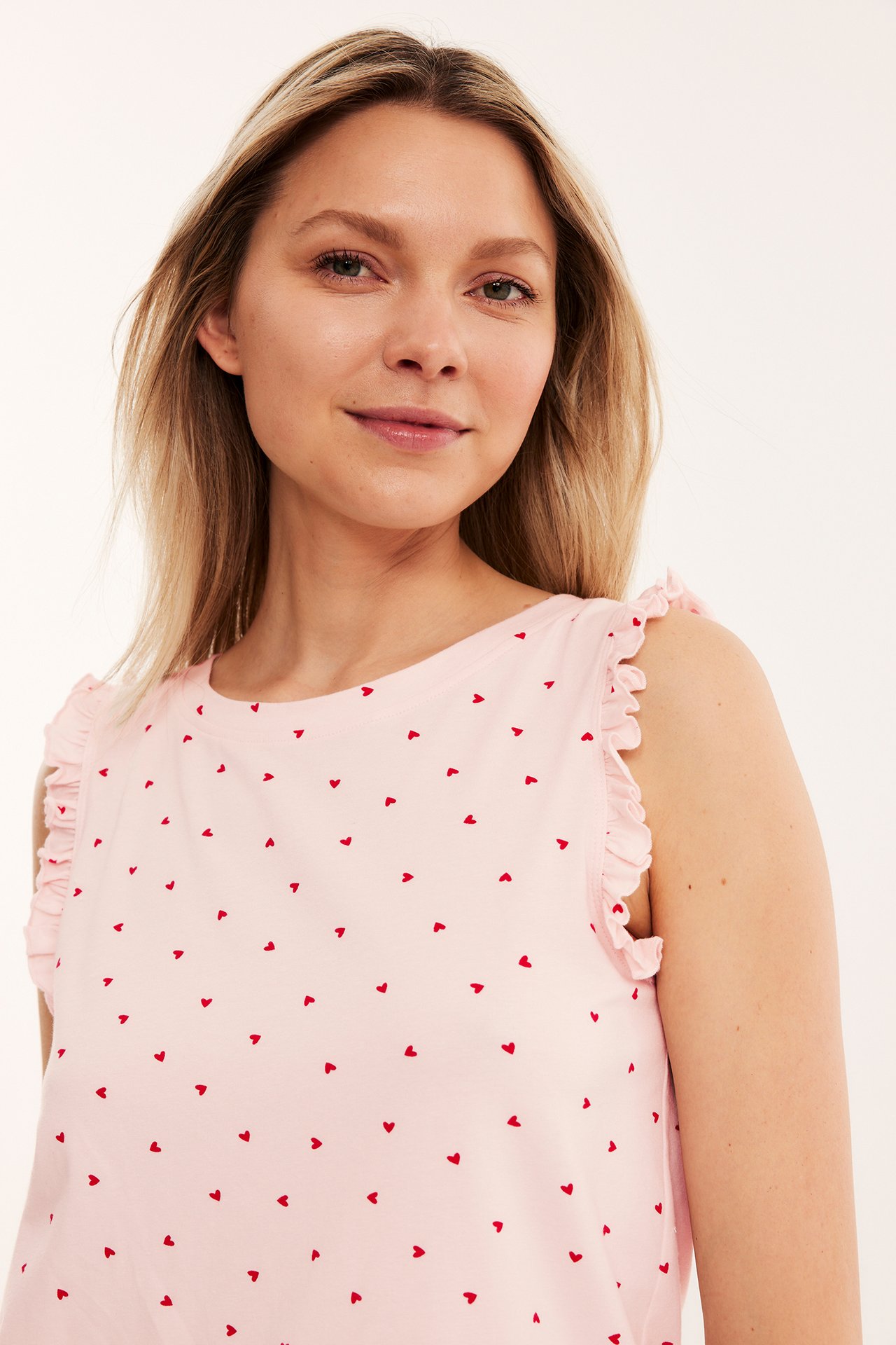 Närbild framifrån på en kvinna i rosa mönstrad pyjamastopp med röda hjärtan och volangärmhål.