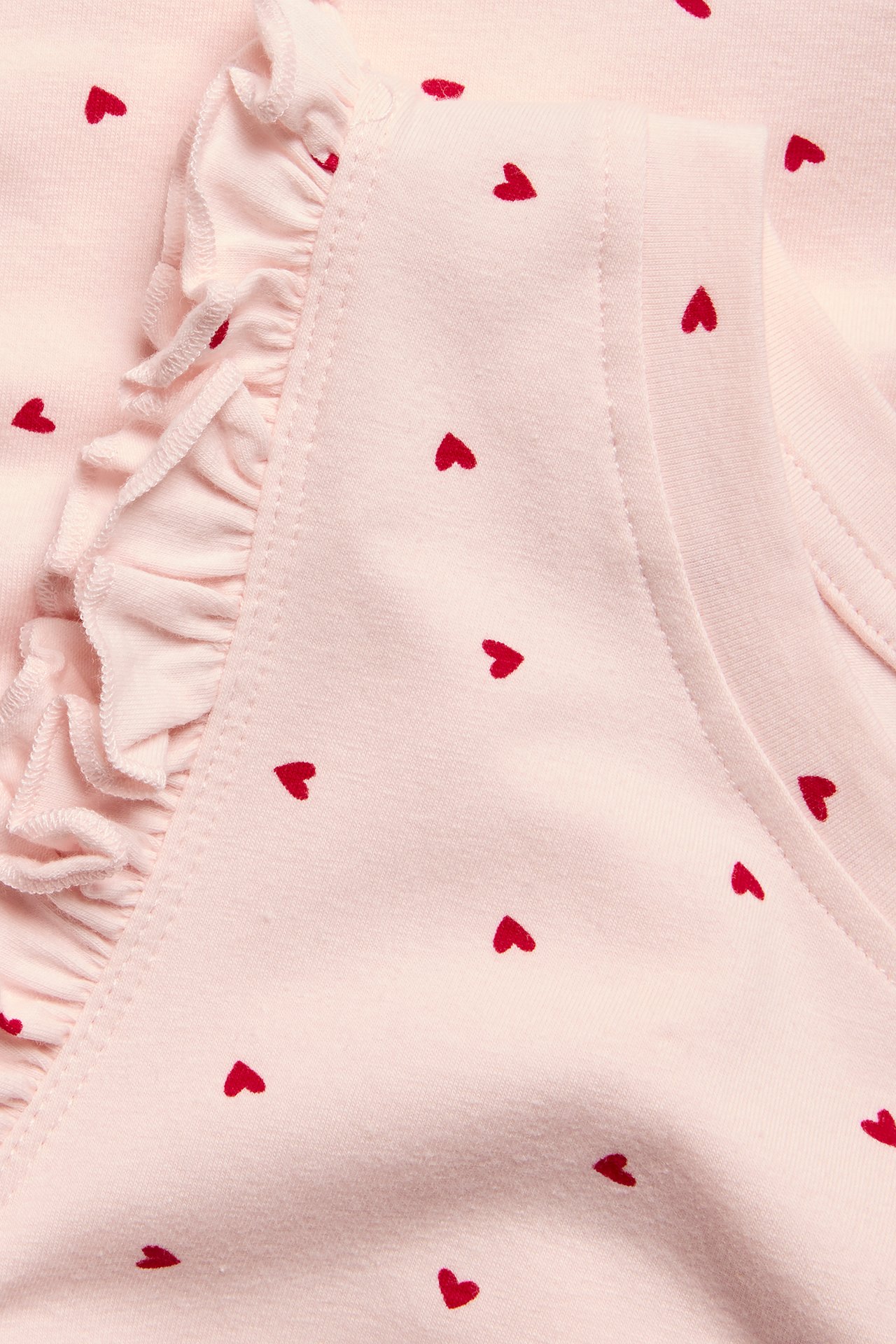 Närbild av rosa mönstrad pyjamas med små röda hjärtan och en volangkant.