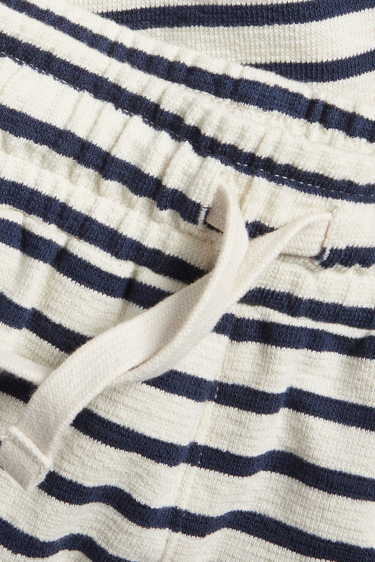 Nærbilde av lysebeige og mørkeblå stripete teksturerte bomullsshorts med snøring i midjen.