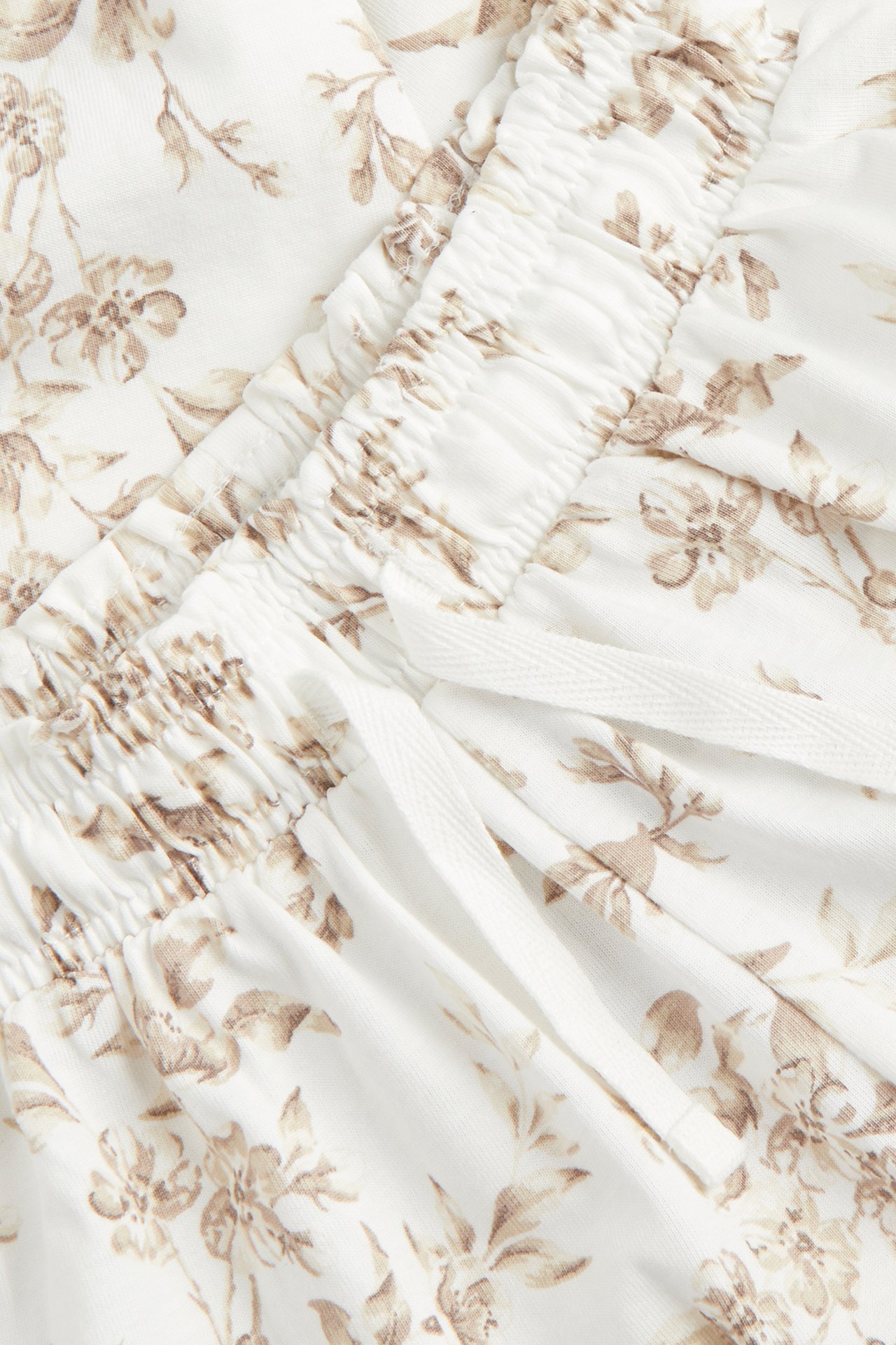 Närbild av offwhite bomullsjerseybyxor med brunt blommigt mönster och resårlinning med dragsko.